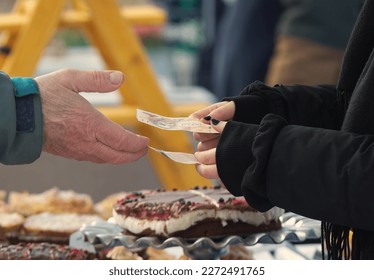 The vendor at the pastry stand accepts payment from the customer for the food sold at street market. Hands holding paper money, cold spring day.
