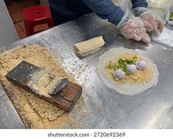 A vendor skillfully rolls a stuffed spring roll filled with ice cream into a cylindrical shape.