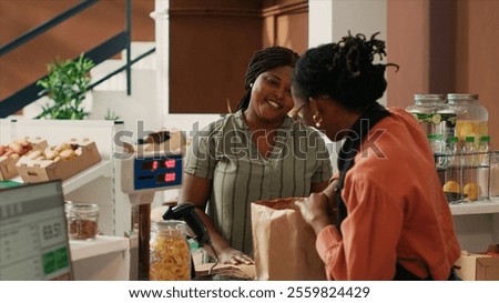 Vendor weighting bulk items for client at cash register, putting natural bio honey jar and chemicals free pasta for vegan woman. Business owner selling organic food to loyal customer.