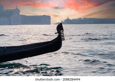 Venetian gondola with traditional iron prow in the shape of a comb sails in the Venice lagoon and Grand Canal at sunset. In the background the Giudecca island and the Church of San Giorgio Maggiore.