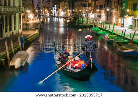 Venetian gondolier punting gondola through green canal waters at night - Venice Italy