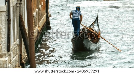 Venetian gondolier punting gondola through green canal waters of Venice Italy.