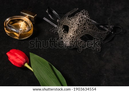 Venetian mask with a red tulip and perfume in a dark, suggestively lit environment. Mysterious love concept, San Valentin day.