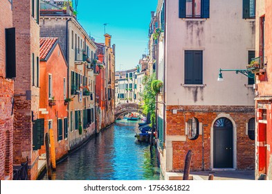 Venice cityscape with narrow water canal with boats moored between old colorful buildings and stone bridge, Veneto Region, Northern Italy. Typical Venetian view, blue sky background