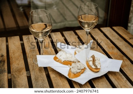 Venice, Italy, 12 February 2023:  Cichetti Venetian tapas with cod mash, cafe restaurant Bacari, Traditional Appetizers snacks accompanied with two glass of white wine, bar food, wooden table