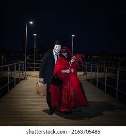 Venice, Italy - 18.02.2022: A Man And A Woman In Venetian Carnival Costumes Standing On Wooden Pier At Grand Canal, Venice At Night