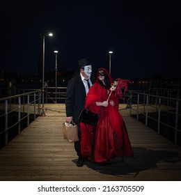 Venice, Italy - 18.02.2022: A Man And A Woman In Venetian Carnival Costumes Standing On Wooden Pier At Grand Canal, Venice At Night