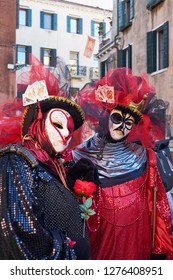 Venice, Italy - February 10, 2018: Couple In Queen Of Hearts And King Of Clubs Black And Red Costumes And White Masks On The Street During The Carnival