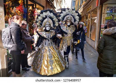 Venice, Italy - February 10, 2018: Couple In White Masks And Black And Gold Costumes On The Street During The Carnival