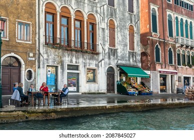 VENICE, ITALY: Group Of Seniors Having Dinner In Outdoor Cafe On Riverfront With Old Houses And Lagoon Around Island Of Giudecca On 5 October 2021. Ancient Italian City Are UNESCO World Heritage Sites