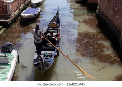 Venice, Italy - June 6 2022: rear and high angle view of a gondolier rowing and carrying a couple of tourists along canals