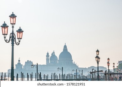 Venice, Italy - October, 2019: Famous venezian street lamps with pink glass in front of Basilica Santa Maria della Salute in Venice in the fog, Italy.