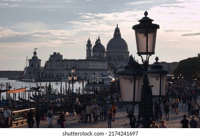 Venice, Italy - September 02, 2018: Gondola boats and street lights against the Basilica of St Mary of Health or Basilica di Santa Maria della Salute at a summer evening with dramatic clouds.