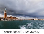 Venice, San Giorgio Maggiore island view from water, from boat. Campanile Bell Tower, Church and lighthouse Faro of San Giorgio Maggiore island with dark blue stormy sky at background.