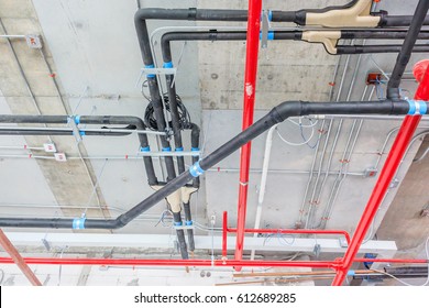 Ventilation pipes in black insulation material and fire sprinkler on red pipe are hanging from the ceiling inside new building factory.