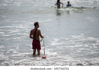 Ventura, California, USA -  June 19, 2020: A lifeguard at Ventura Harbor enters the ocean from the shore with his rescue equipment, including floatation device and fins.