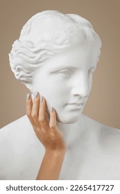 Venus sculpture with human woman's hand on beige background