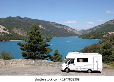 Verdon Gorge France. Lac De Castillon. Motor Home Camping Car Parked Alongside Turquoise Blue Lake With Rugged Green Hills Under A Blue Sky.  