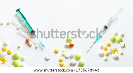Verity of colorful medicial pills spilling out of the glass jar and bottle with syringe on white background. Medical concept.