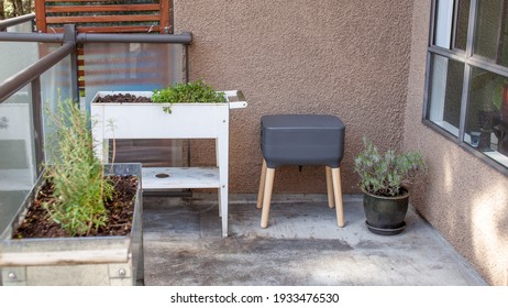 A vermicomposting system (worm composter) sits on an apartment balcony with other patio planters. Worms eat food scraps and produce worm castings and worm tea to be used as fertilizer