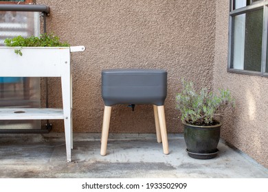A vermicomposting system (worm composter) sits on an apartment balcony with other patio planters. Worms eat food scraps and produce worm castings and worm tea to be used as fertilizer