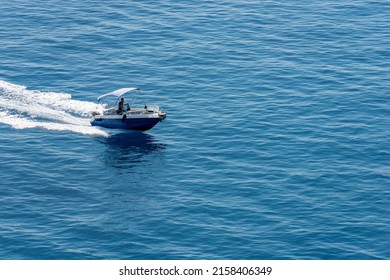 VERNAZZA, ITALY - JULY 22, 2019: Small Blue Motor Boat With One Person On Board Runs Fast In The Blue Mediterranean Sea With White Wake, Photographed From Above. Cinque Terre, Liguria, Italia, Europe