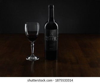 Vero Beach, Florida; USA; Dec. 7, 2020. A Bottle Of A Red Wine Blend Accompanies A Tasting Glass Of The Poured Wine In A Glass  At The Center Of A Rosewood Table. The Image Has Dark And Moody Lighting