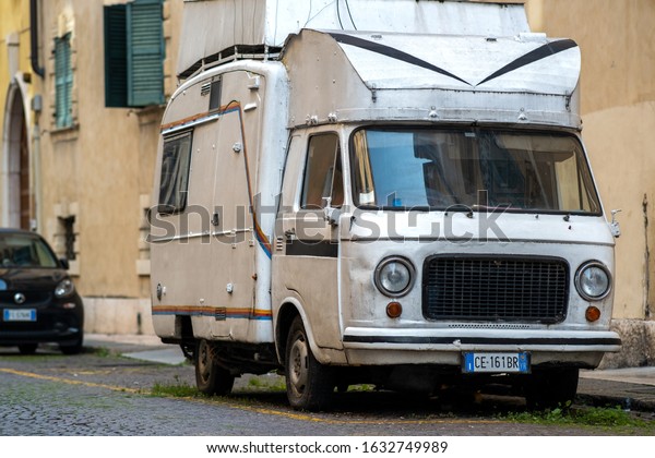 Verona, Italy -\
October 21, 2019: Old camper car parked on city street side in\
residential discrict. Shiny vehicles parked by the curb. Urban\
transportation infrastructure\
concept.