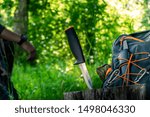 Versatile all around compact camping knife ideal for backpack tours with vivid colors and a person in the background in a campsite.