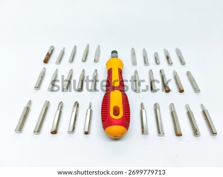 Versatile multi bit screwdriver with a red and yellow handle, surrounded by an assortment of interchangeable metal tips on a clean white surface Some bits show signs of light corrosion and use