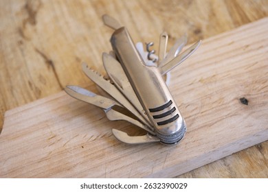 A versatile silver multi-tool knife with several blades and tools extended, lying on a textured wooden surface