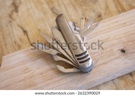 A versatile silver multi-tool knife with several blades and tools extended, lying on a textured wooden surface