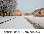 Verschneite Straße und beleuchtete Gebäude der Staatsoper Unter den Linden und Humboldt-Universität in Berlin an einem winterlichen Abend.