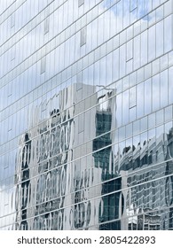 Vertical abstract shot capturing a distorted wavy architectural reflection of an adjacent building on the glossy glass window wall facade of a skyscraper.