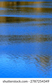 Vertical abstract view of dark and light blue reflections dancing on the surface of calm water.