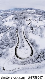 A Vertical Aerial Shot Of A Beautiful Winter Landscape With A Long Winding Road In The Countryside