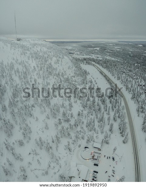 A vertical aerial shot of buildings and cars in a\
winter forest