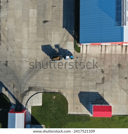 A vertical aerial view of a blue Belorus tractor transporting cargo (fodder, manure, fertilizer) on a farm. Trace of tractor wheels on concrete. Tractor rides on the territory of the enterprise.