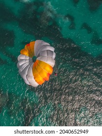 A Vertical Aerial View Of A Person Parasailing Over The Turquoise Sea