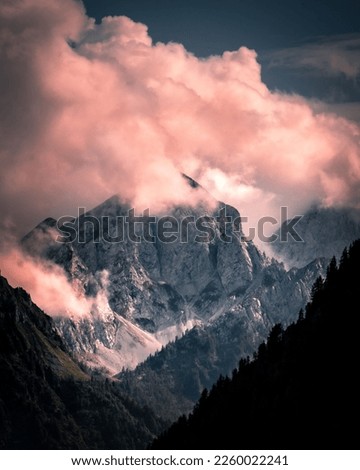 A vertical aerial view of a rocky peak of a green mountain range covered with clouds at sunset
