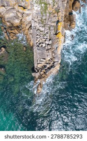Vertical aerial view of a solid rocky pier extending into clear green ocean water