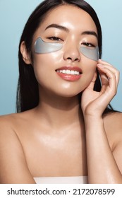 Vertical Of Asian Beauty Woman Uses Under Eye Patches, Mask From Dark Circles And Puffiness, Cleansing Her Face, Stands Over Blue Background