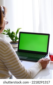 Vertical Back Over Shoulder View Of Elderly Woman With Glasses Watching Educational Webinar, Online Lecture Seminar On Laptop With Green Screen, Taking Notes. The Concept Of Distance Education.