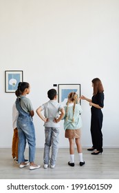 Vertical Back View At Diverse Group Of Children Listening To Female Tour Guide While Visiting Modern Art Gallery