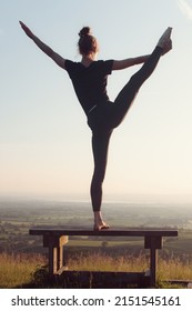 A Vertical Back View Of A Female Doing An Acrobatic Yoga Stretch Outdoors At Sunset