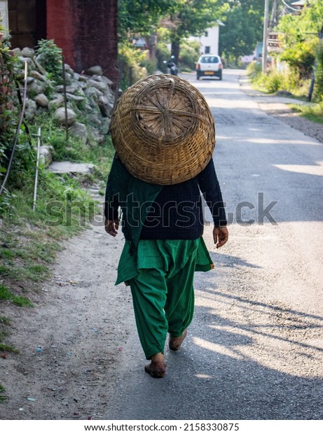 A vertical back view of a man carrying a\
basket on his back walking on the\
street