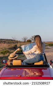 Vertical Back View Of Unrecognizable Women Sitting And Reading A Map In A Red Retro Convertible Car Wit Copy Space