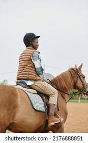 Vertical Back View At Young Woman Riding Horse In Ranch And Wearing Helmet