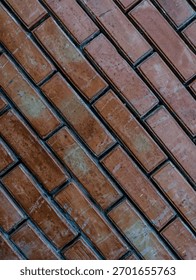 Vertical background texture of a rustic brick wall arranged in a strong diagonal pattern. The aged red and brown clay bricks provide an industrial, weathered architectural