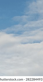 Vertical background of thick fluffy white clouds gathering against a blue sky with copy space on top.